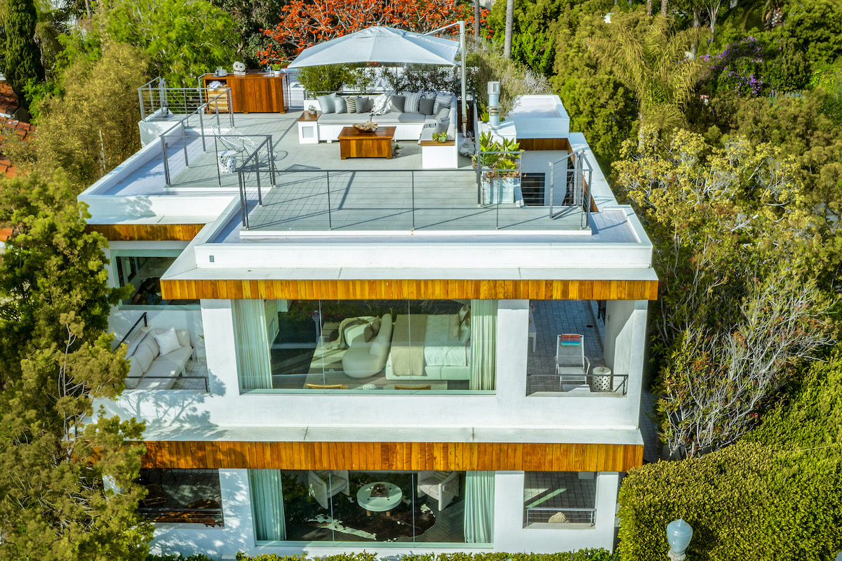 aerial view of a three-story home with a rooftop deck surrounded by trees