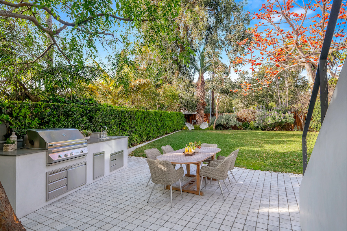 backyard patio with grassy lawn, table and chairs, bbq and sink, and a staircase leading upstairs