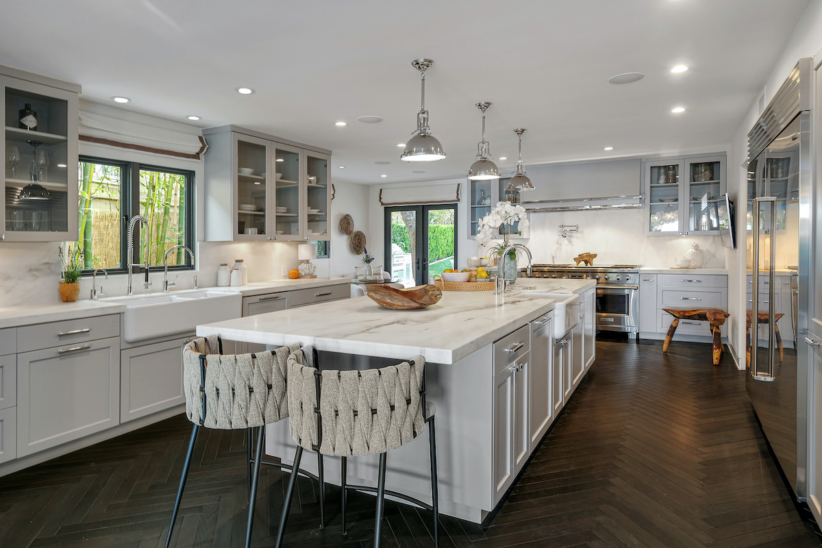 kitchen with a large island with white marble countertops, 2 bar stools, grey cabinets, and a stainless steel fridge