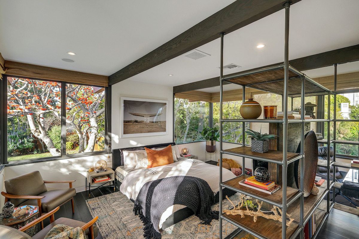 bedroom with windows on all walls, a bed in the middle of the room, and metal shelving with plants