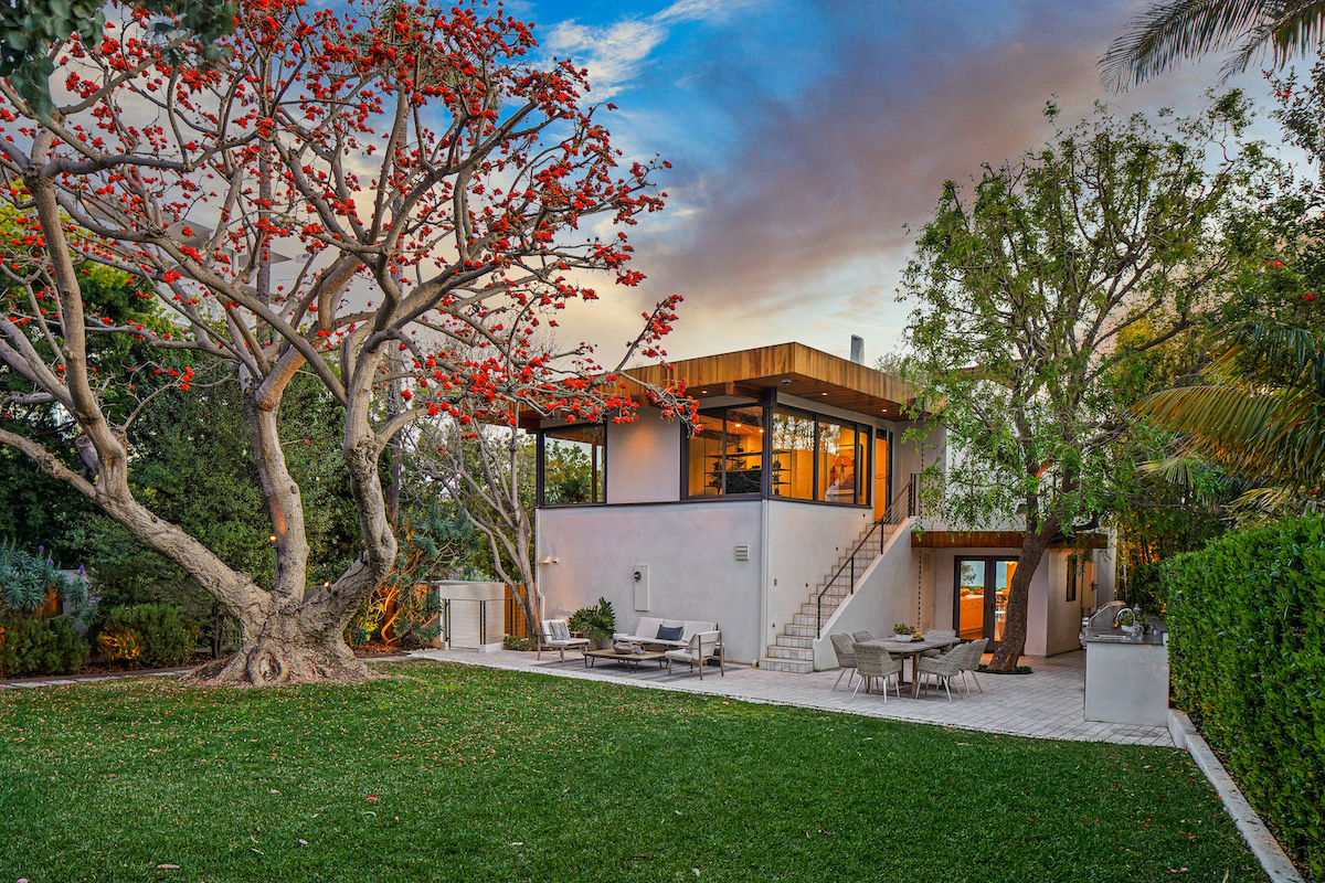 grassy backyard showing the back of a house with staircase leading to the back door and an outdoor patio