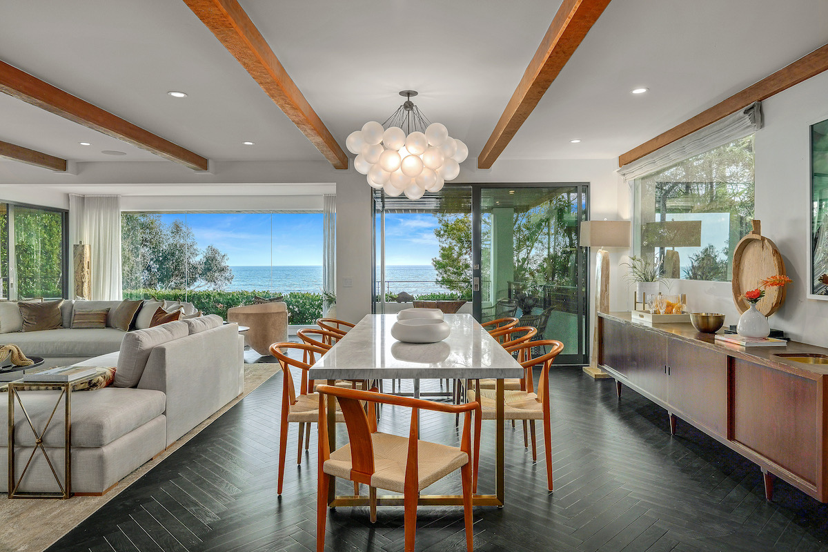 dining room with chairs around a marble table in front of windows showing an ocean view, and a couch to the left