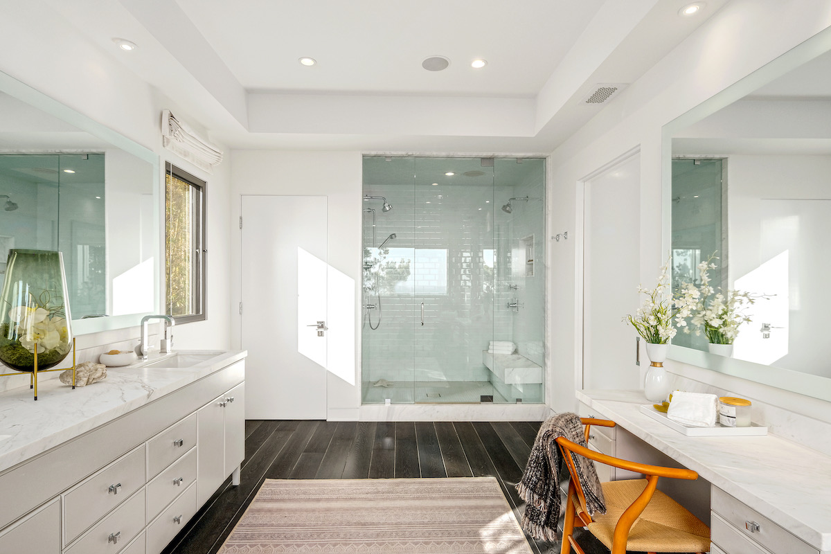 bathroom with luxury shower, dual marble sink countertop, and vanity with a wooden chair