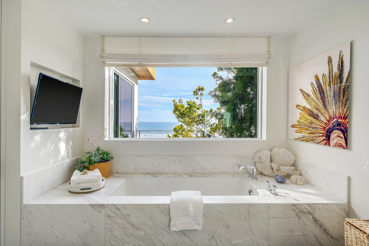 master bathroom white marble tub with a tv on the wall, and window showing ocean views