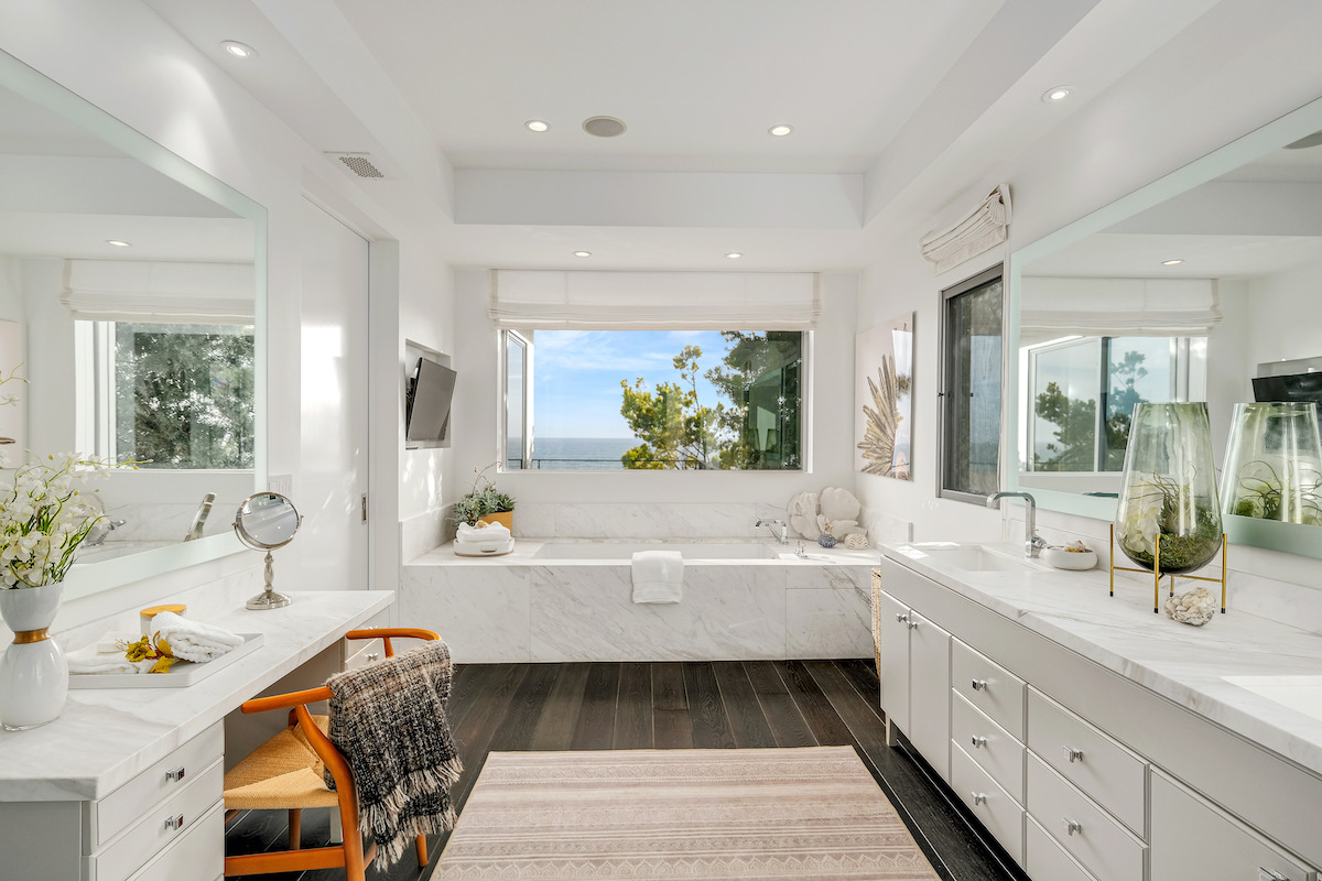 master bathroom white marble tub with a tv on the wall, vanity and sink area, and window showing ocean views