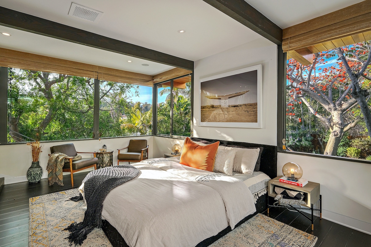 bedroom with windows on all walls showing the lush backyard, with 2 chairs and bed in the middle in the room