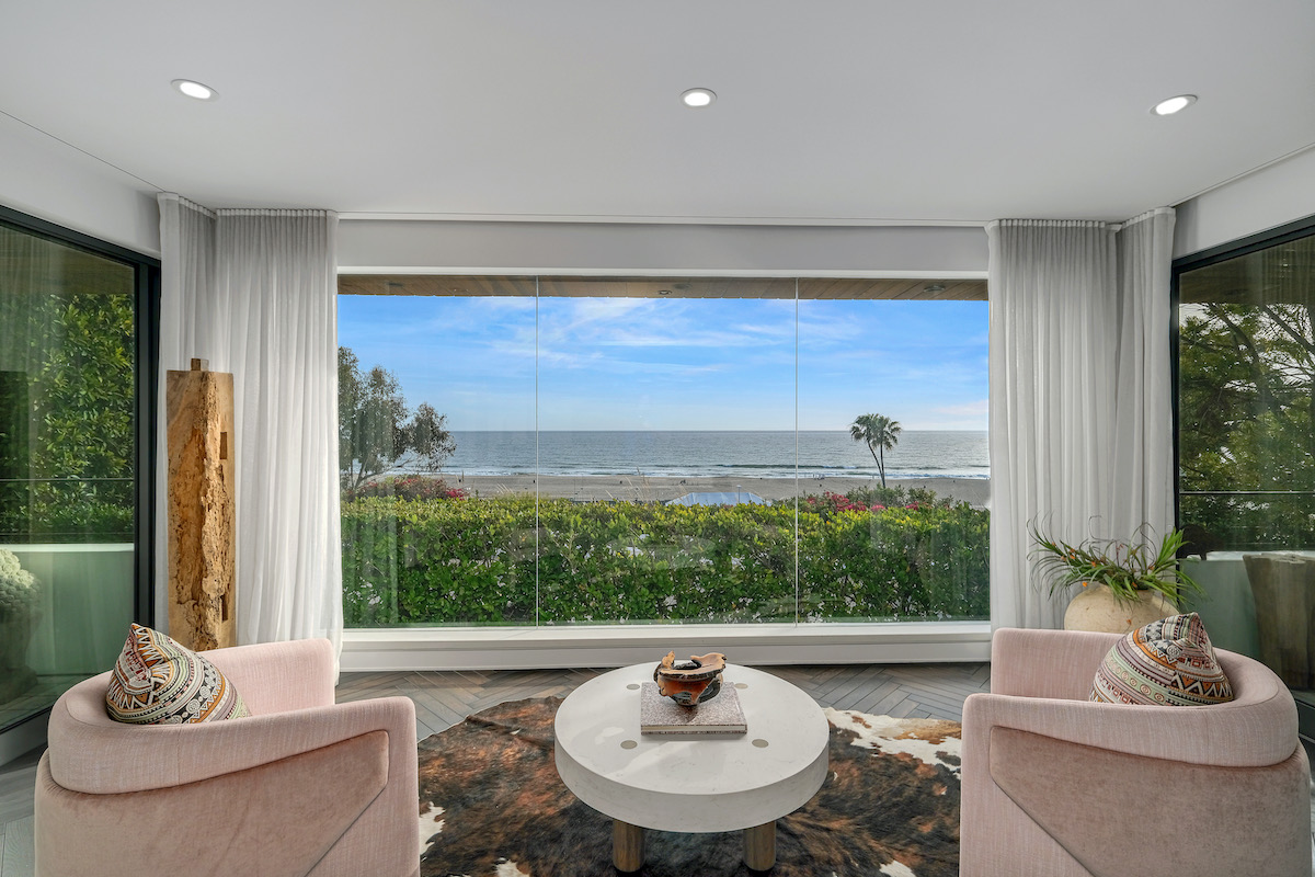 a sitting area with 2 chairs and a table, sitting in front of a floor-to-ceiling window showing ocean views