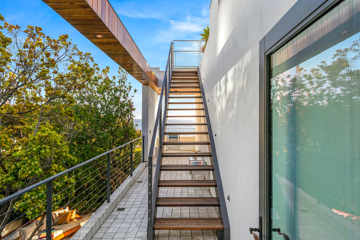 staircase on the side of a house leading to the rooftop with ocean views in the distance