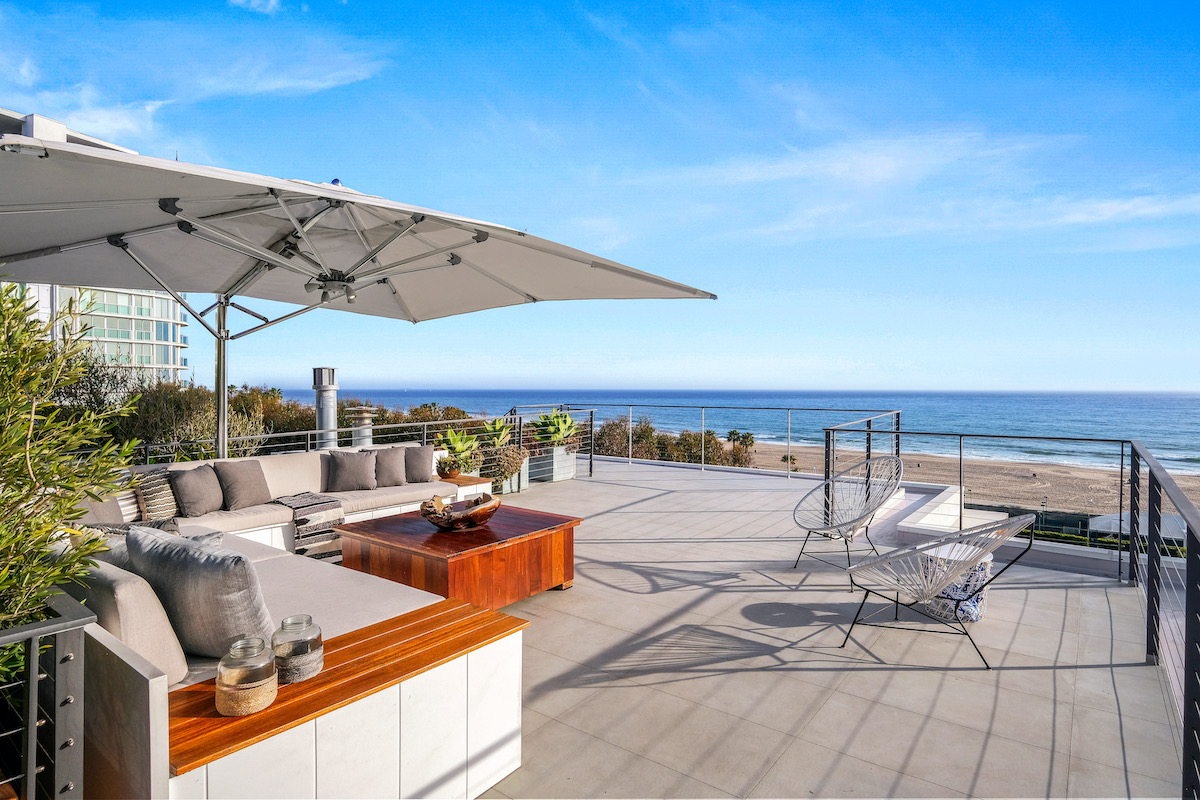 rooftop deck with a couch, wooden table, chairs, and umbrella looking at oceanfront views