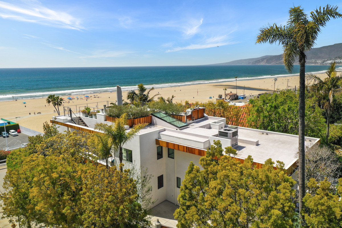 aerial shot of a beachfront home on the sand surrounded by trees and palms