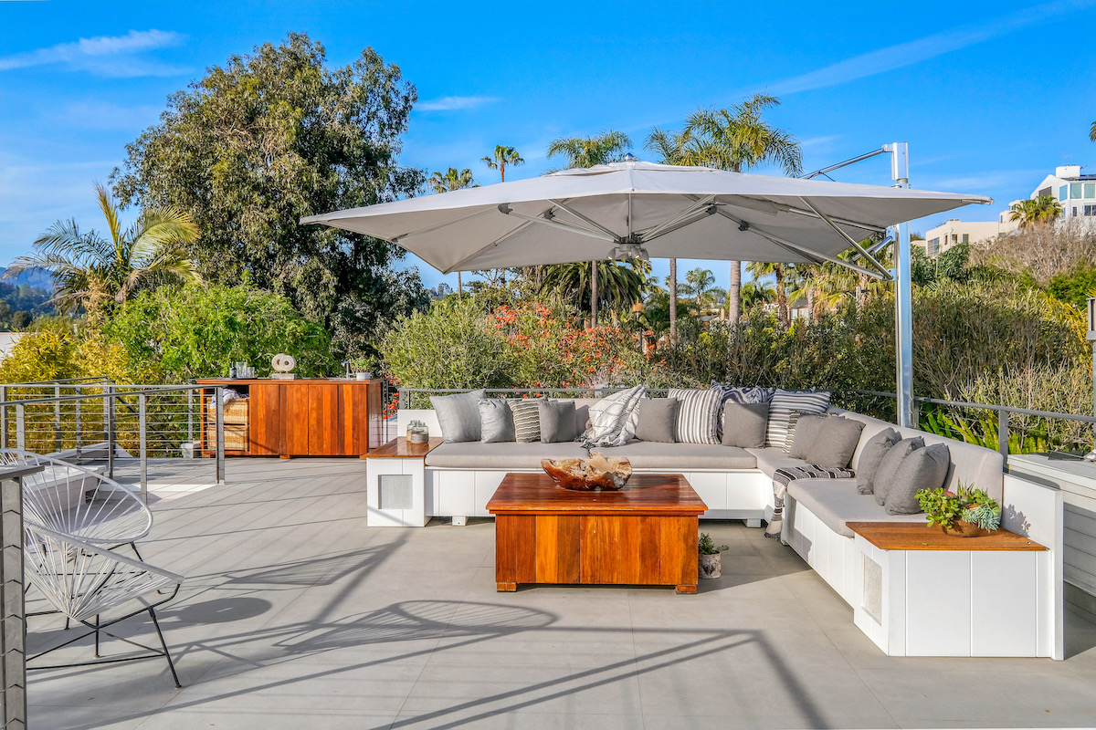 rooftop outdoor patio area with L-shaped couch, wooden table and umbrella